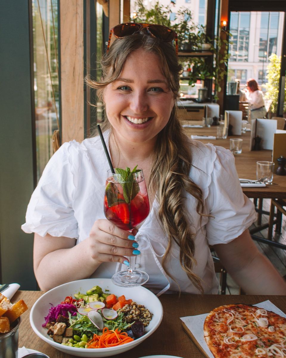 Elise smiling with a red spritz over salad and pizza