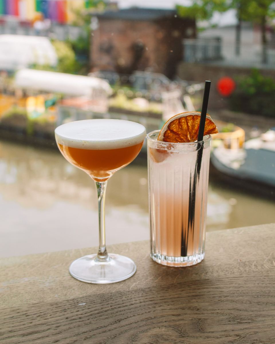 Two cocktails on a wooden ledge overlooking a canal
