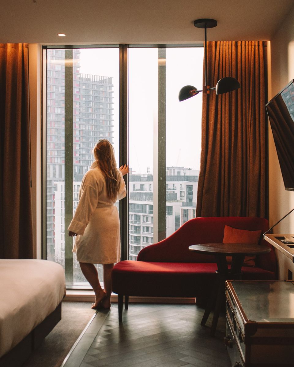 Woman in a robe looking out of a floor-to-ceiling hotel window