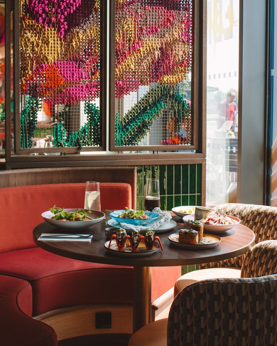 Hotel restaurant table set with small plates beside a vibrant beaded art wall