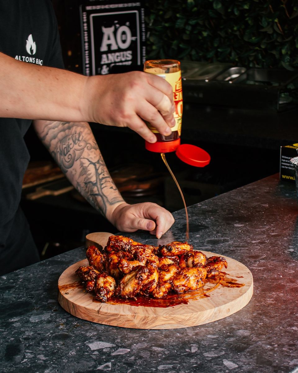 Hot honey being drizzled over a board of glazed chicken wings